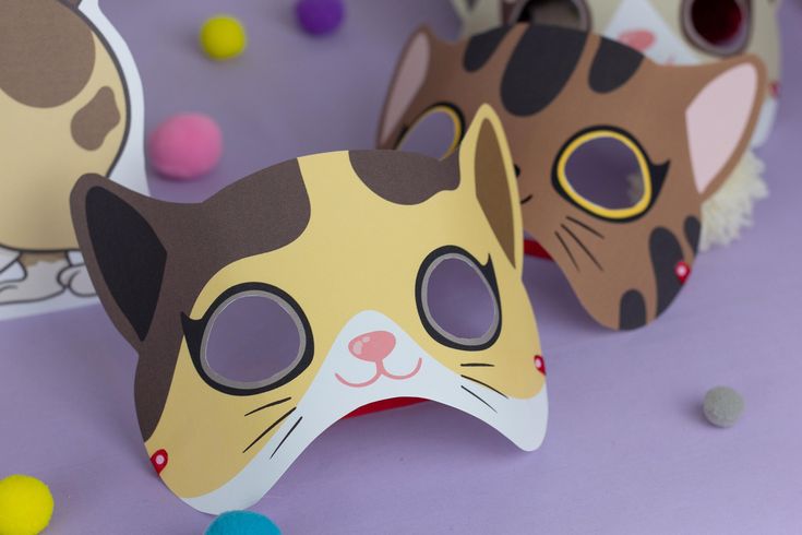 two paper masks with cats on them sitting next to some balls and confetti