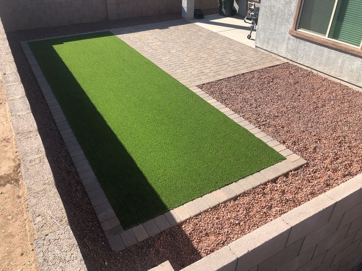 an artificial grass lawn in front of a house with gravel and pavers on the ground