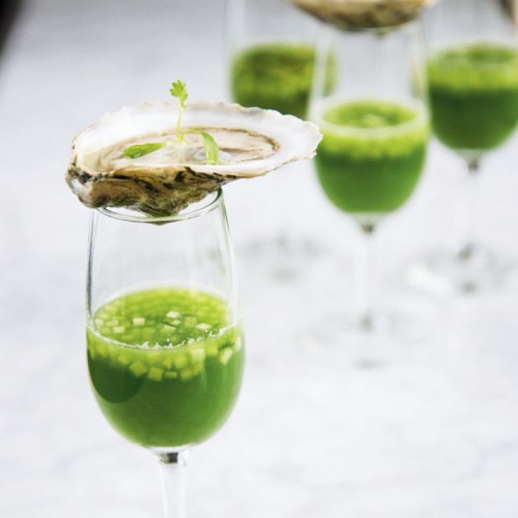 three wine glasses filled with green liquid and some oysters on the table in front of them