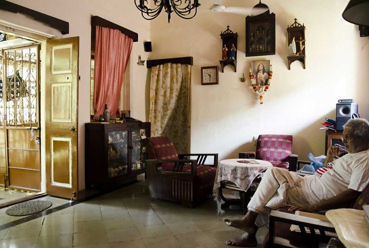 an old man sitting in a living room next to a doorway and some pictures on the wall