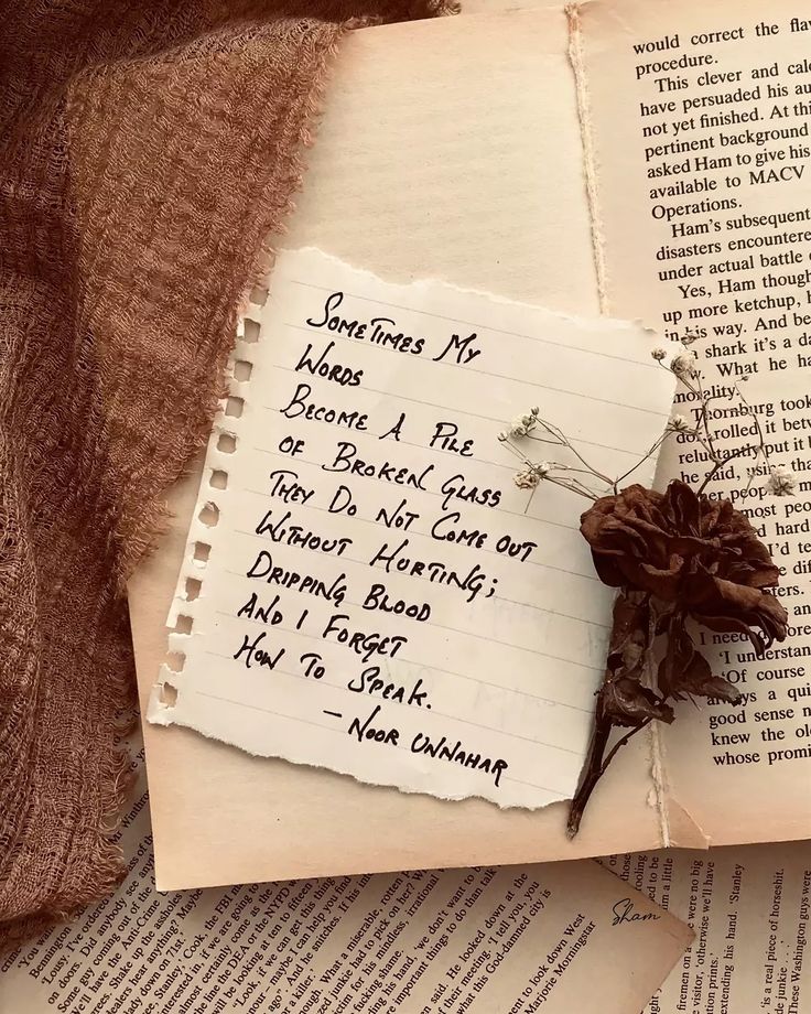 a piece of paper with writing on it next to an open book and a dried flower