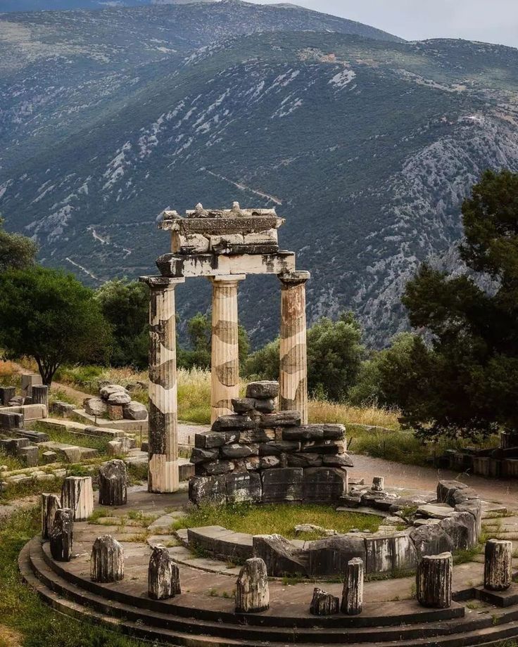 an old roman temple in the middle of a field with trees and mountains behind it