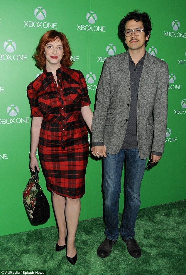 a man and woman standing next to each other in front of a green wall holding hands