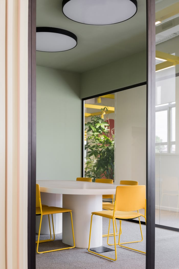 an office meeting room with yellow chairs and a round white table surrounded by green walls