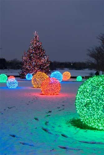 lighted balls in the snow with a christmas tree in the backgroung behind them