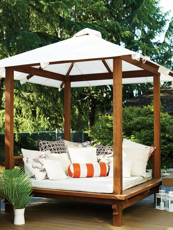 an outdoor day bed with white cushions and pillows on it's sides, surrounded by greenery