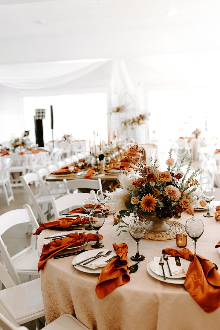 the table is set with white chairs and orange napkins