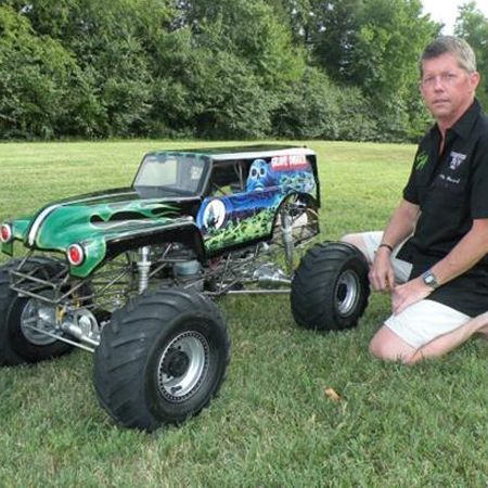 a man sitting in the grass next to a monster truck