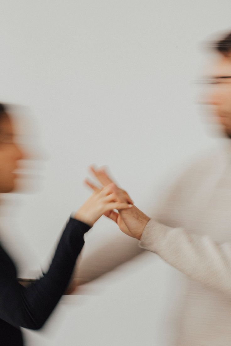 two people standing next to each other in front of a white wall with blurry hands