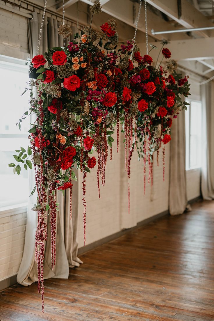 red flowers are hanging from the ceiling in an empty room with wooden floors and drapes