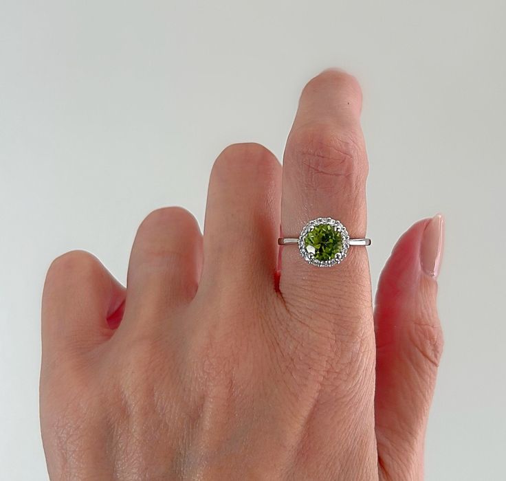 a woman's hand holding a ring with a green gemstone in the middle