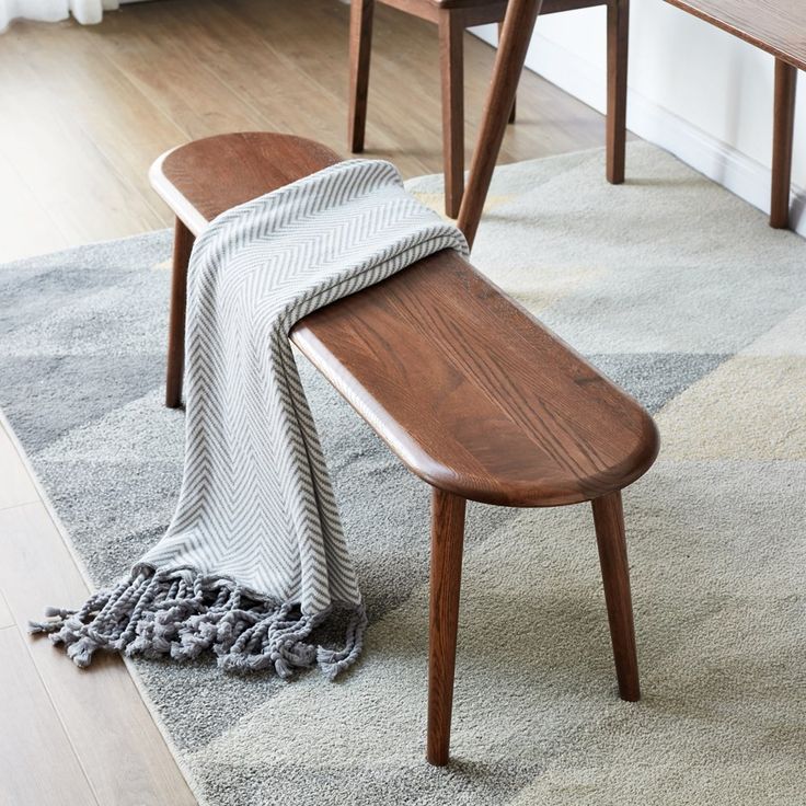 a wooden bench sitting on top of a rug next to a chair and table with a blanket