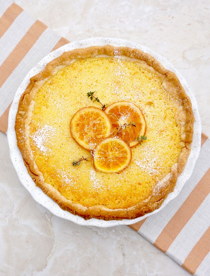 a pie with slices of oranges on top in a white dish next to a striped table cloth