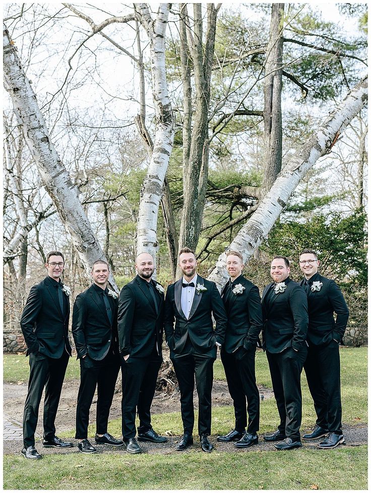 a group of men standing next to each other in front of some trees and grass