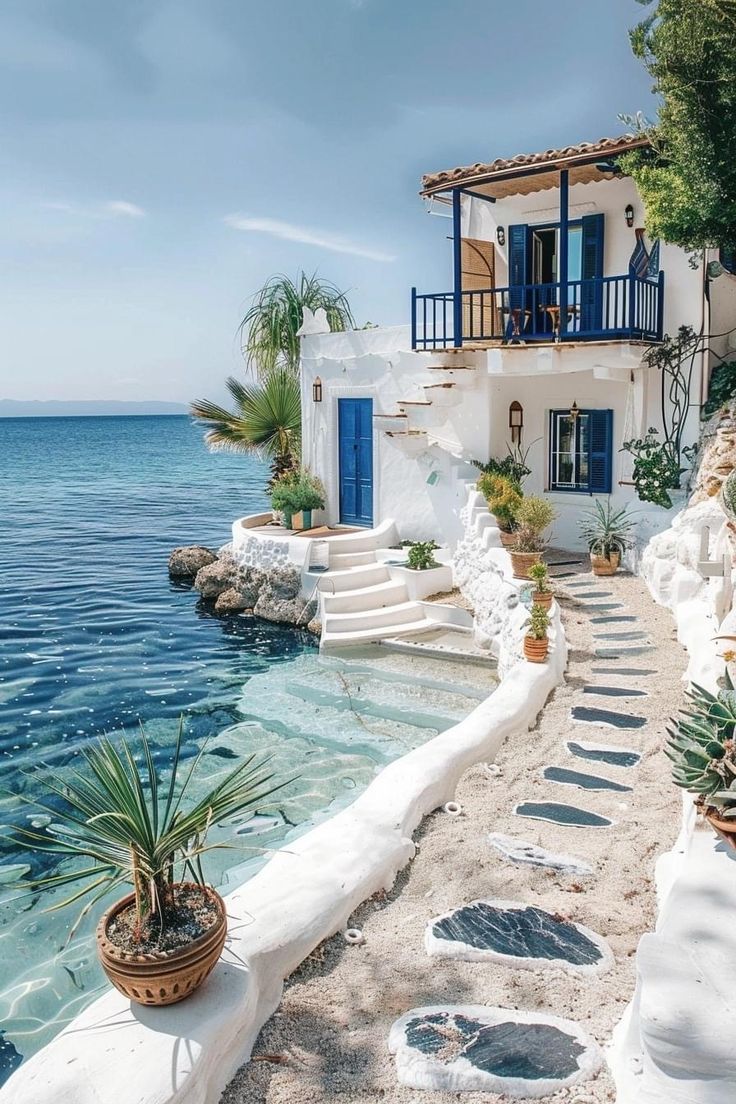 a white house with blue shutters next to the ocean and steps leading up to it