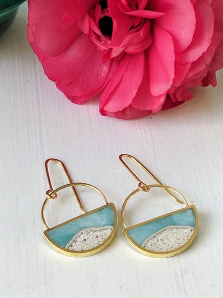 two gold hoop earrings with blue and white designs on them next to a pink flower