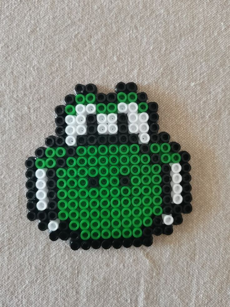 a green and black beaded brooch sitting on top of a white cloth