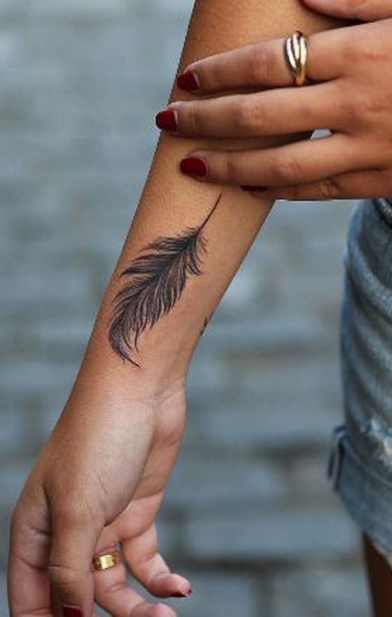 two hands holding each other with tattoos on their wrists and fingers, one has a feather tattoo on it's left arm