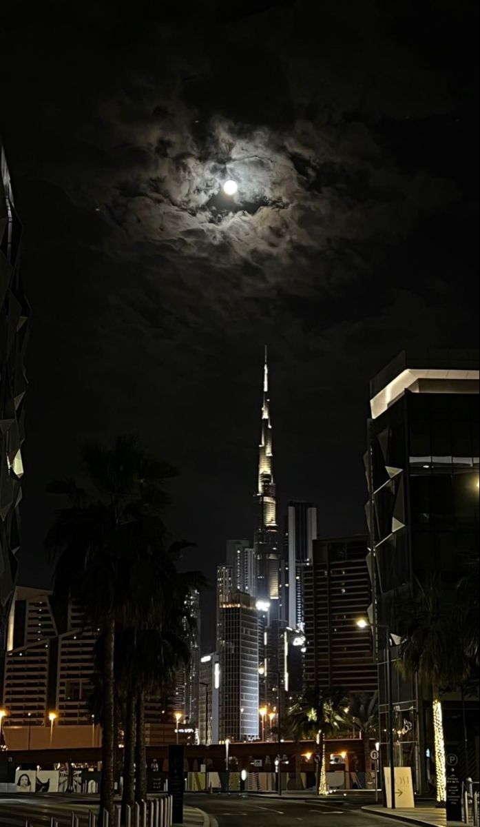 a full moon is seen over a city at night with skyscrapers in the background