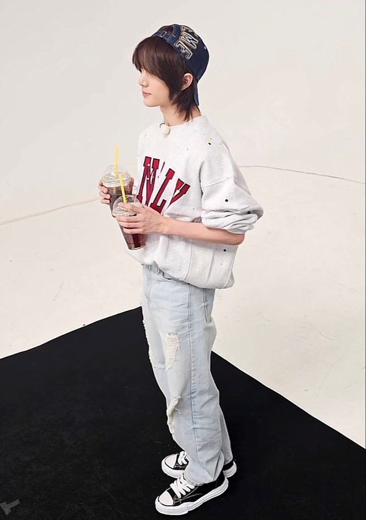 a young boy is holding a drink and wearing a baseball uniform while standing on a black carpet