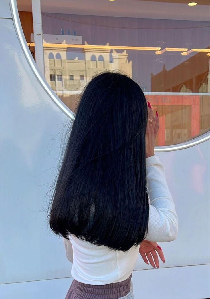 a woman with long black hair standing in front of a building looking out the window