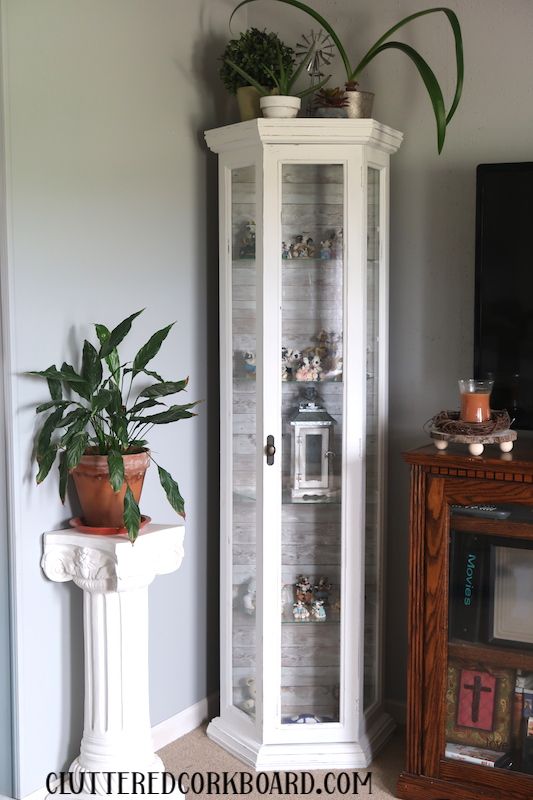 a tall white corner cabinet with plants on top