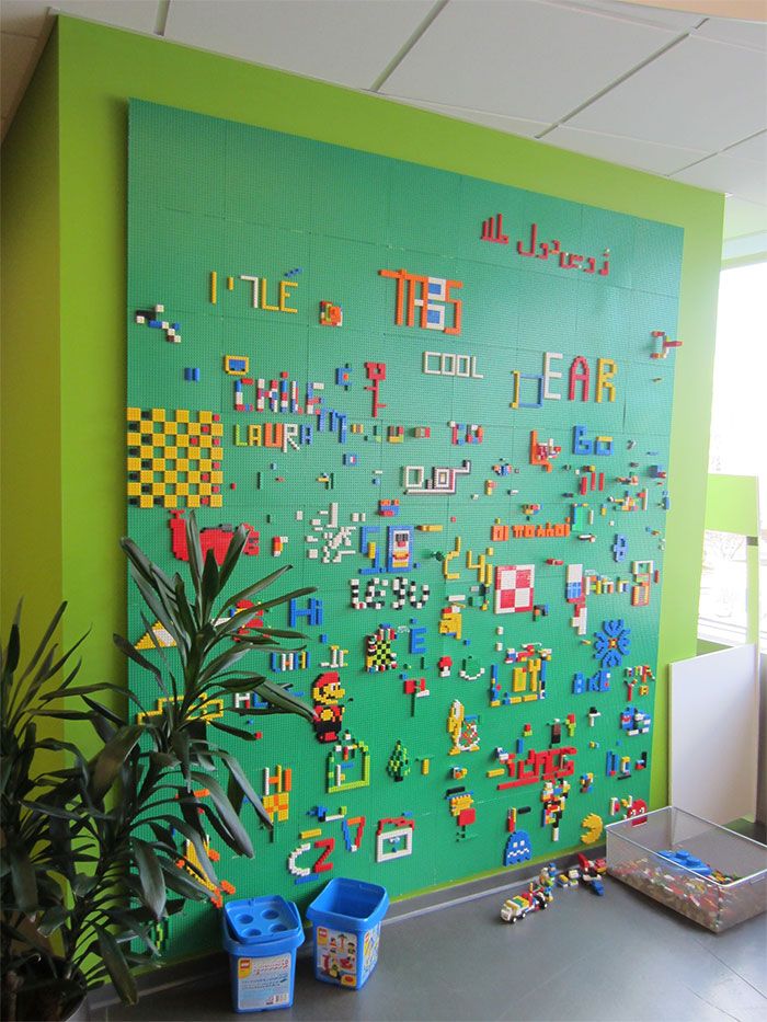 a green wall covered in lots of legos next to a potted plant on top of a table