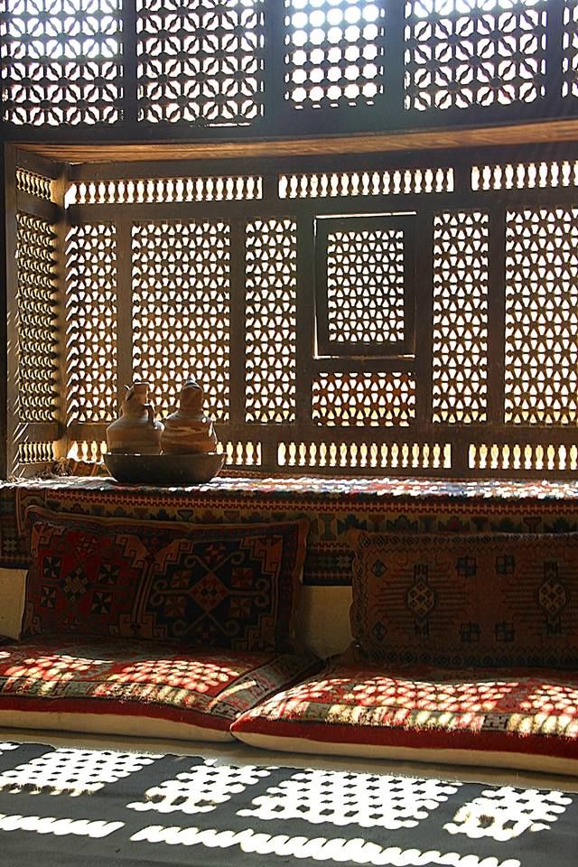 the sun shines through an intricately designed window and onto a bench with pillows on it