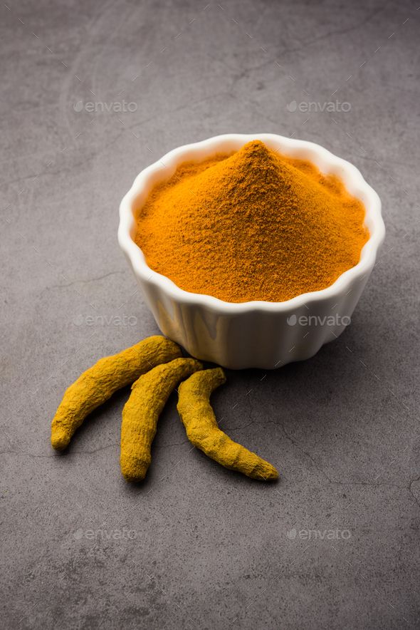 a white bowl filled with yellow powder next to two banana peels on a gray surface