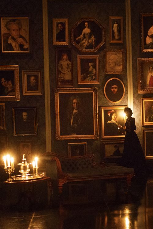 a woman standing in front of a room with pictures on the wall and candles lit