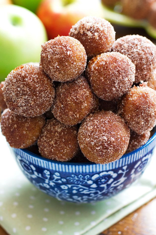 a blue bowl filled with sugar covered donuts on top of a table next to apples