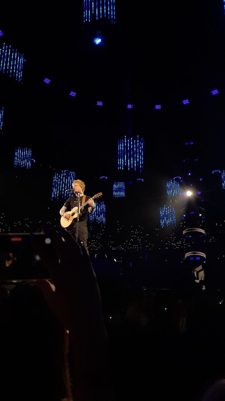 a man that is standing on a stage with a guitar in his hand and lights behind him