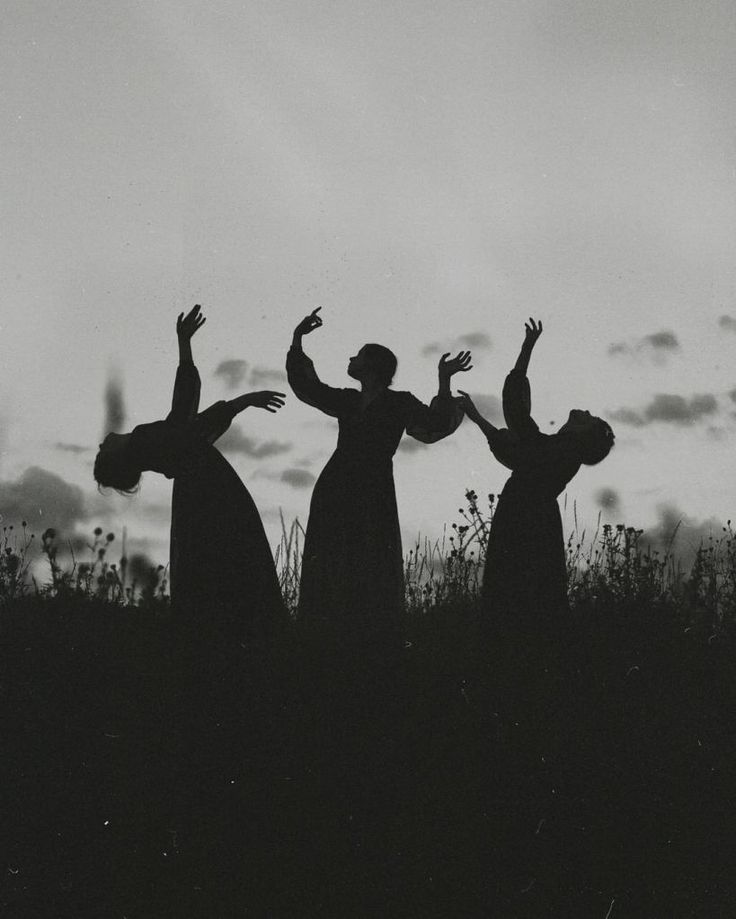 three people standing on top of a grass covered field with their arms in the air