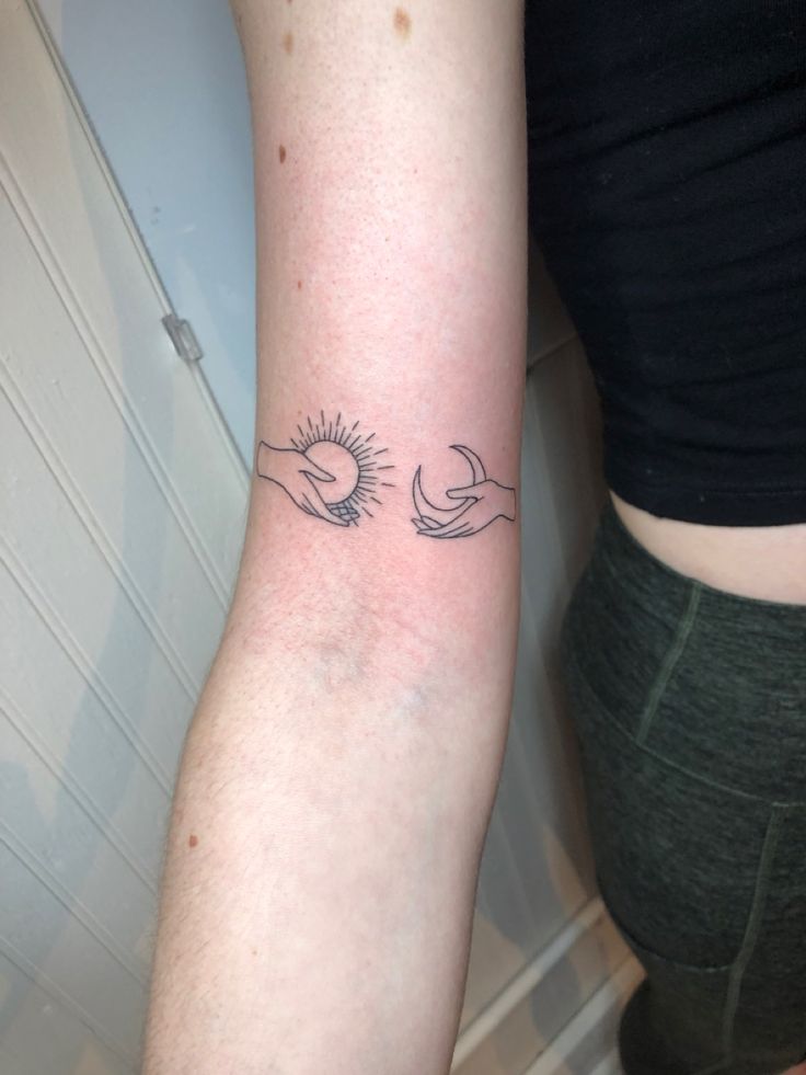 two hands holding each other with the sun and moon tattoo on their arm, behind them is a woman's leg