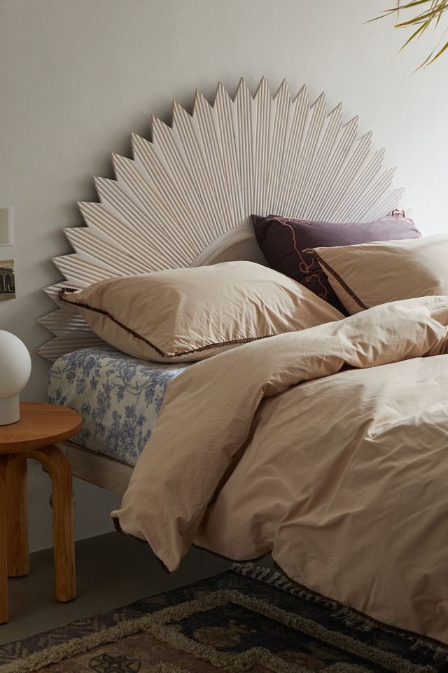 a bed with beige sheets and pillows on top of it next to a small table