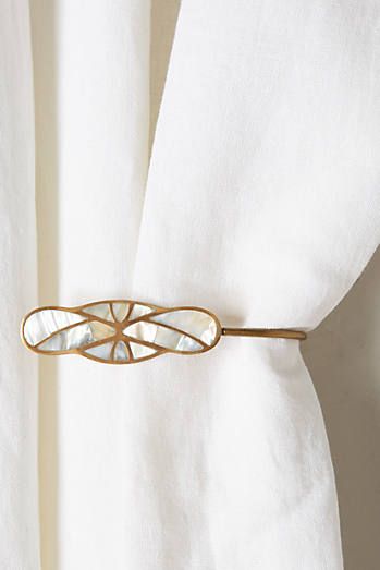 a close up of a white curtain with a gold tie pin on it's side