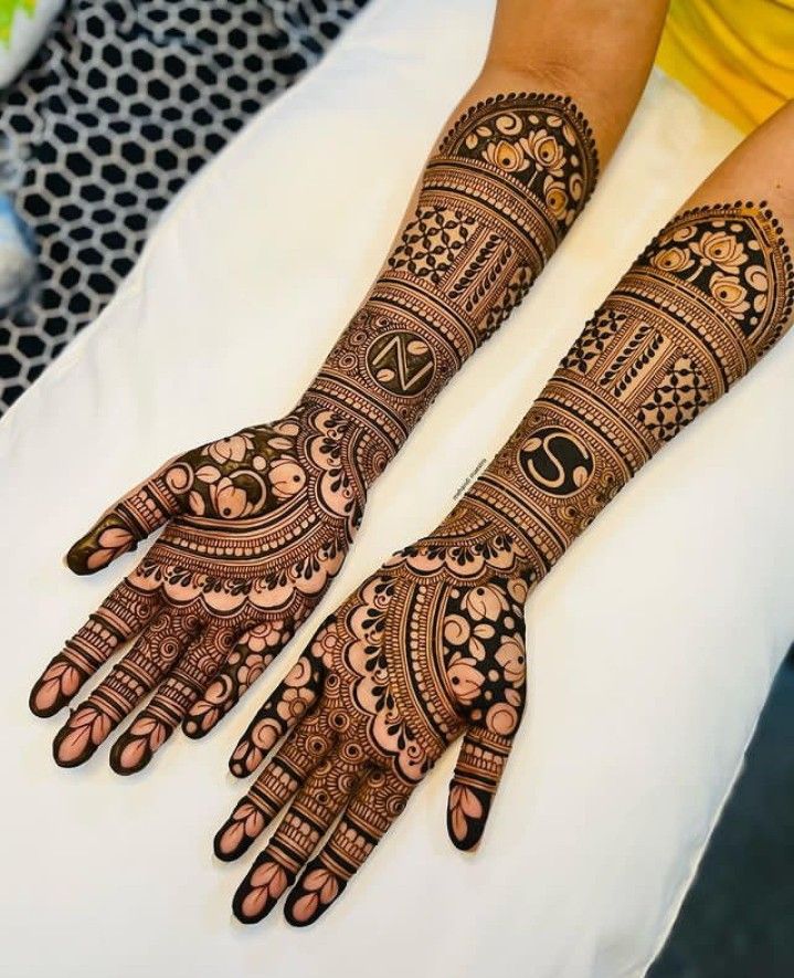 two hands with henna designs on them sitting on a white sheet in front of a woman's face