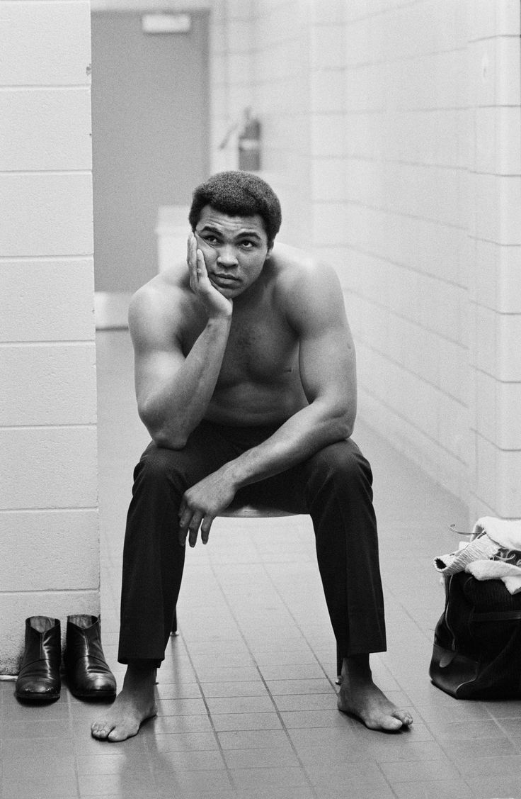 a shirtless man sitting on a toilet talking on a cell phone in a bathroom