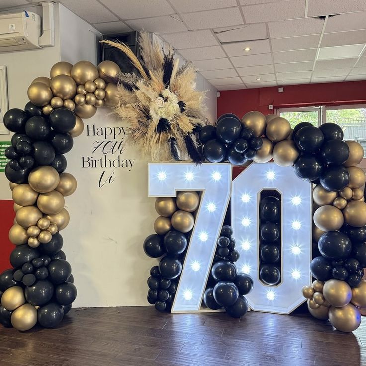 a large balloon arch with the number seventy on it in front of a happy 70th birthday sign