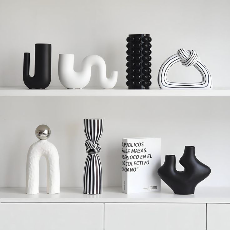 some black and white vases sitting on top of a white shelf next to each other