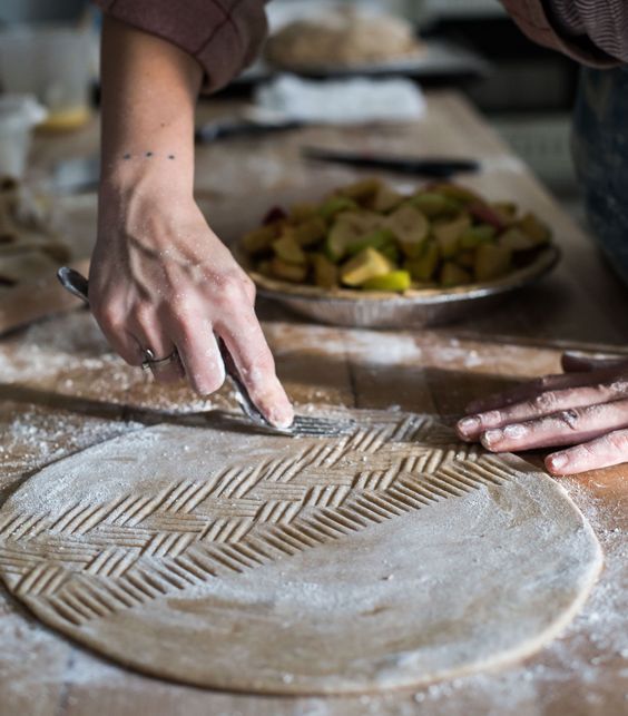 a person is cutting dough on a table with other food items in the back ground