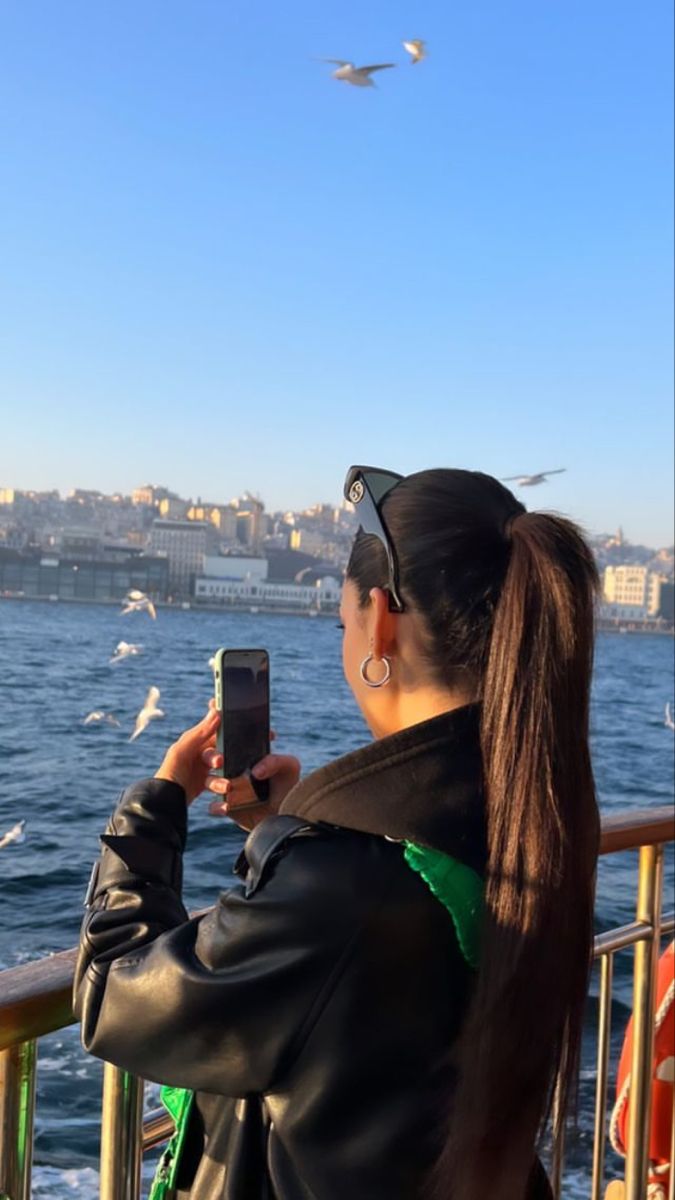 a woman taking a photo of seagulls flying over the water from a boat