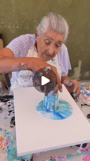 an older woman is painting on a table with blue and white paint in front of her