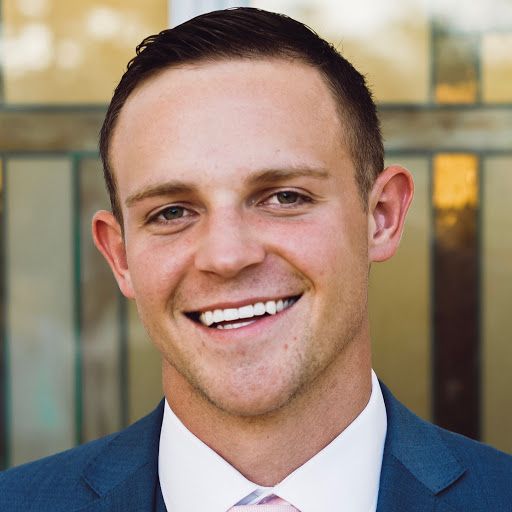 a man in a suit and tie smiling at the camera with a glass door behind him