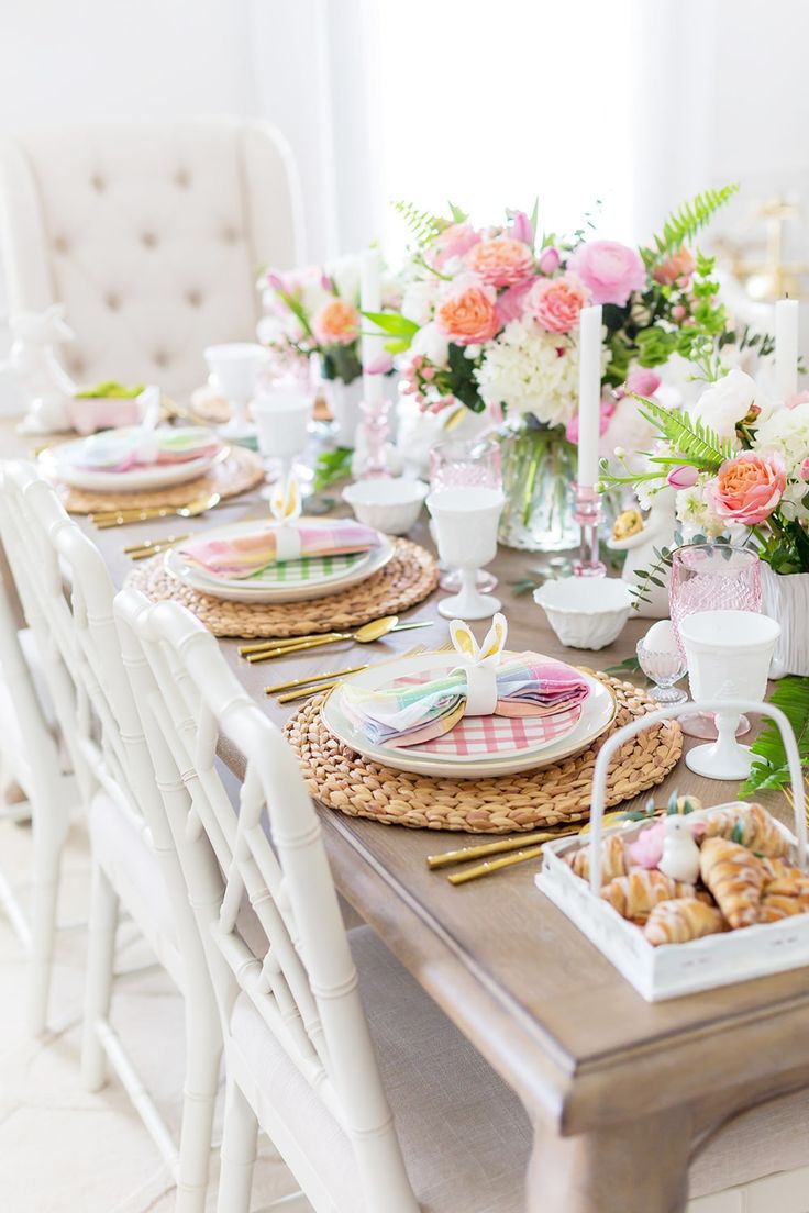 the table is set with pink and white flowers in vases, plates, cups, and napkins