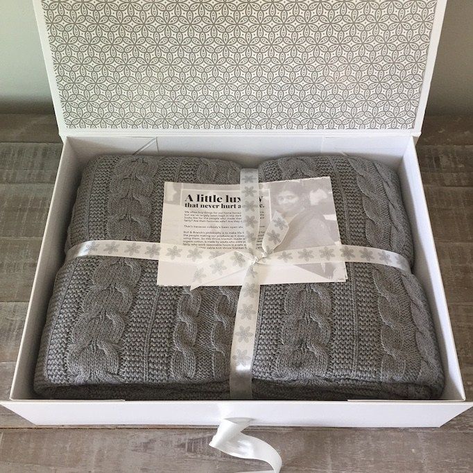 a box with two blankets wrapped in grey and white cable knits, tied with a white ribbon