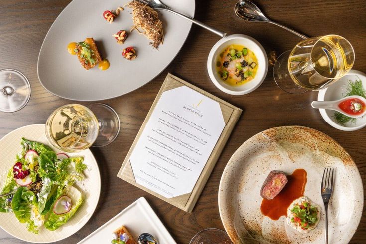 an assortment of food and drinks on a table with menus, wine glasses and utensils