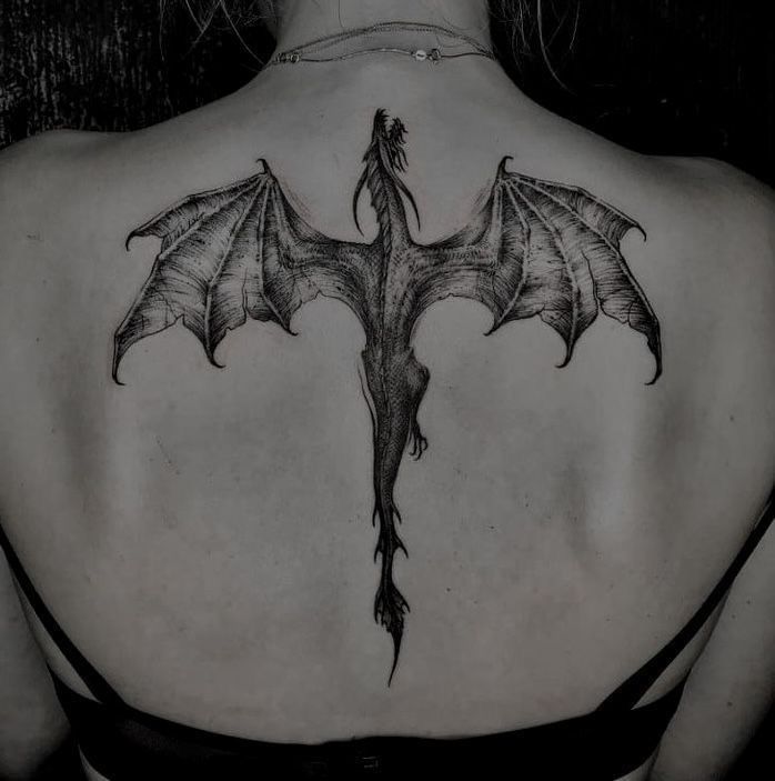 the back of a woman's shoulder with a dragon tattoo on it, and wings