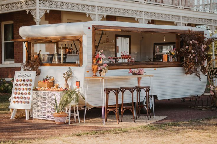 an old fashioned mobile home is parked in front of a building with flowers on display