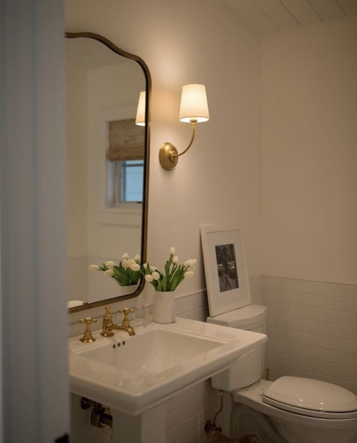 a white toilet sitting next to a sink under a bathroom mirror with flowers on it